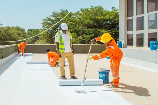 Technician applying waterproofing membrane to building foundation for structural protection